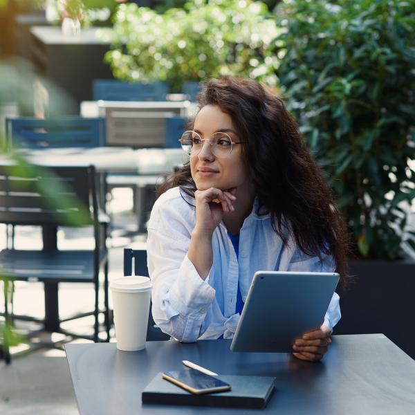 woman holding a tablet while having a coffee