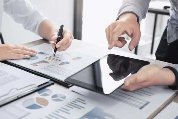 hands holding a tablet on a table full of paper reports