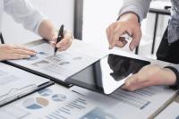 hands holding a tablet on a table full of paper reports